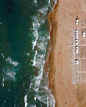 High-angle view of a beach with waves, sunbeds, and umbrellas. Perfect summer vacation spot.
