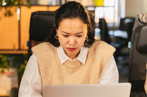 Free Woman concentrating on laptop in office, showcasing focus and productivity. Stock Photo