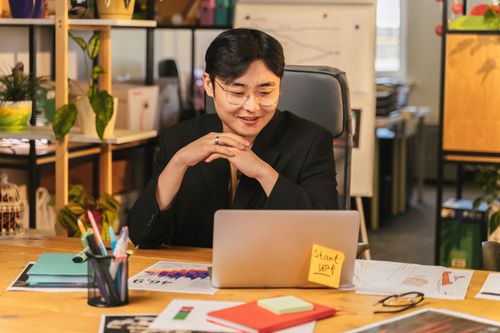 Free Asian man working happily in a modern office with a laptop, representing startup culture. Stock Photo
