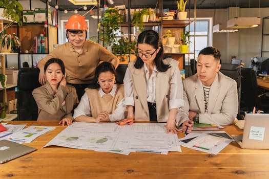 Diverse team collaborating on a project at a desk in a modern office environment with charts and plans.