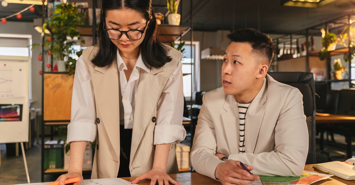 Two colleagues engaged in a focused discussion in a modern office setting with plants and documents.