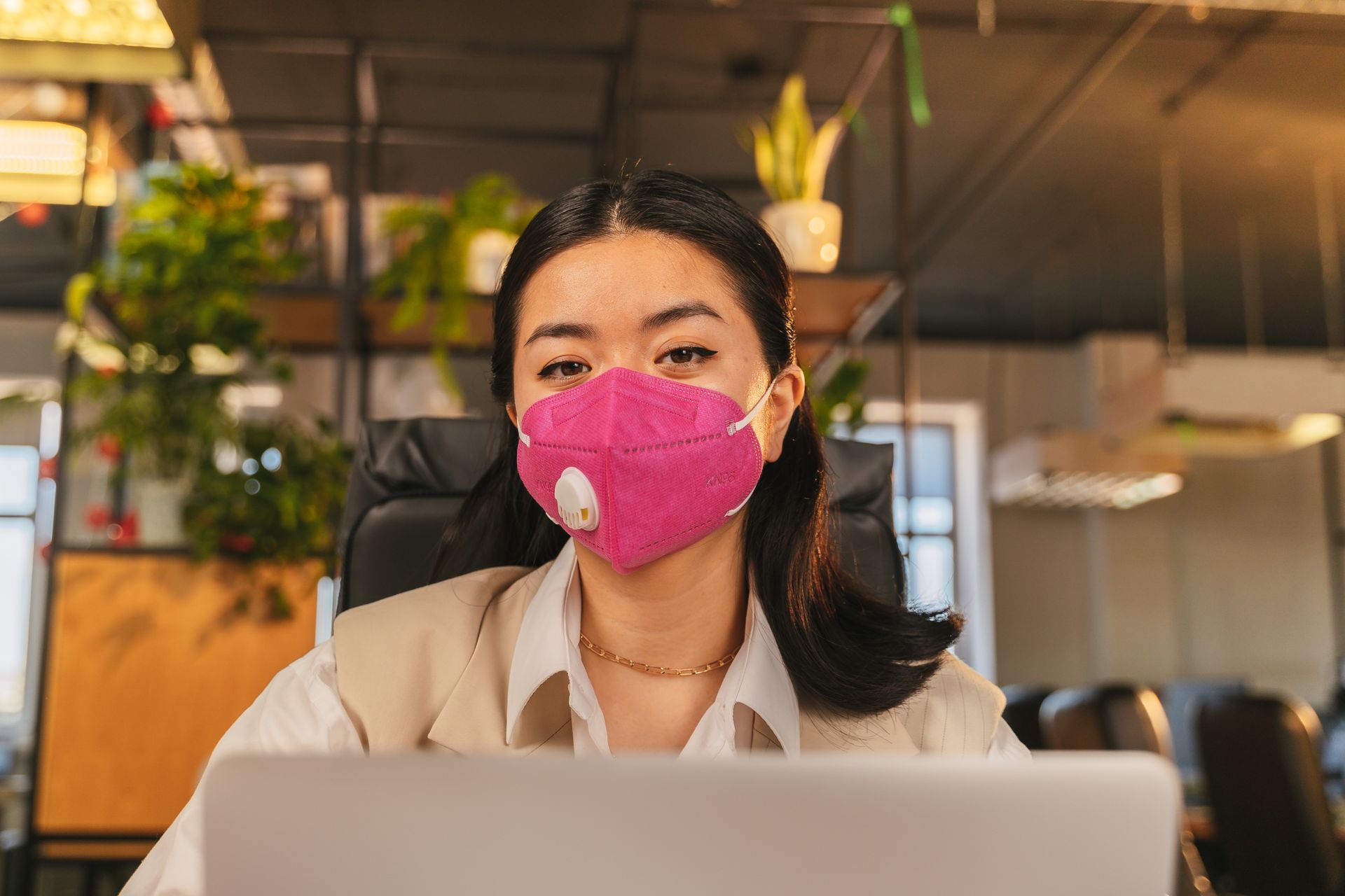 Asian woman in an office setting wearing a protective pink face mask, symbolizing the new normal workplace environment.