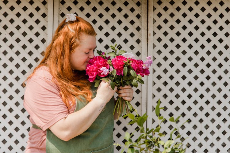 A Woman In Pink Shirt Smelling Flowers With Her Eyes Closed