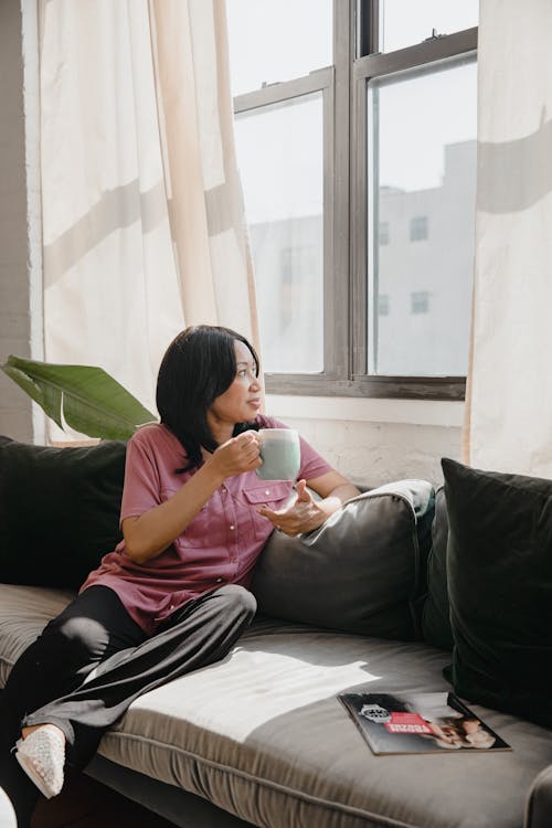 A Woman in Pink Shirt Sitting on the Couch while Looking at the Window