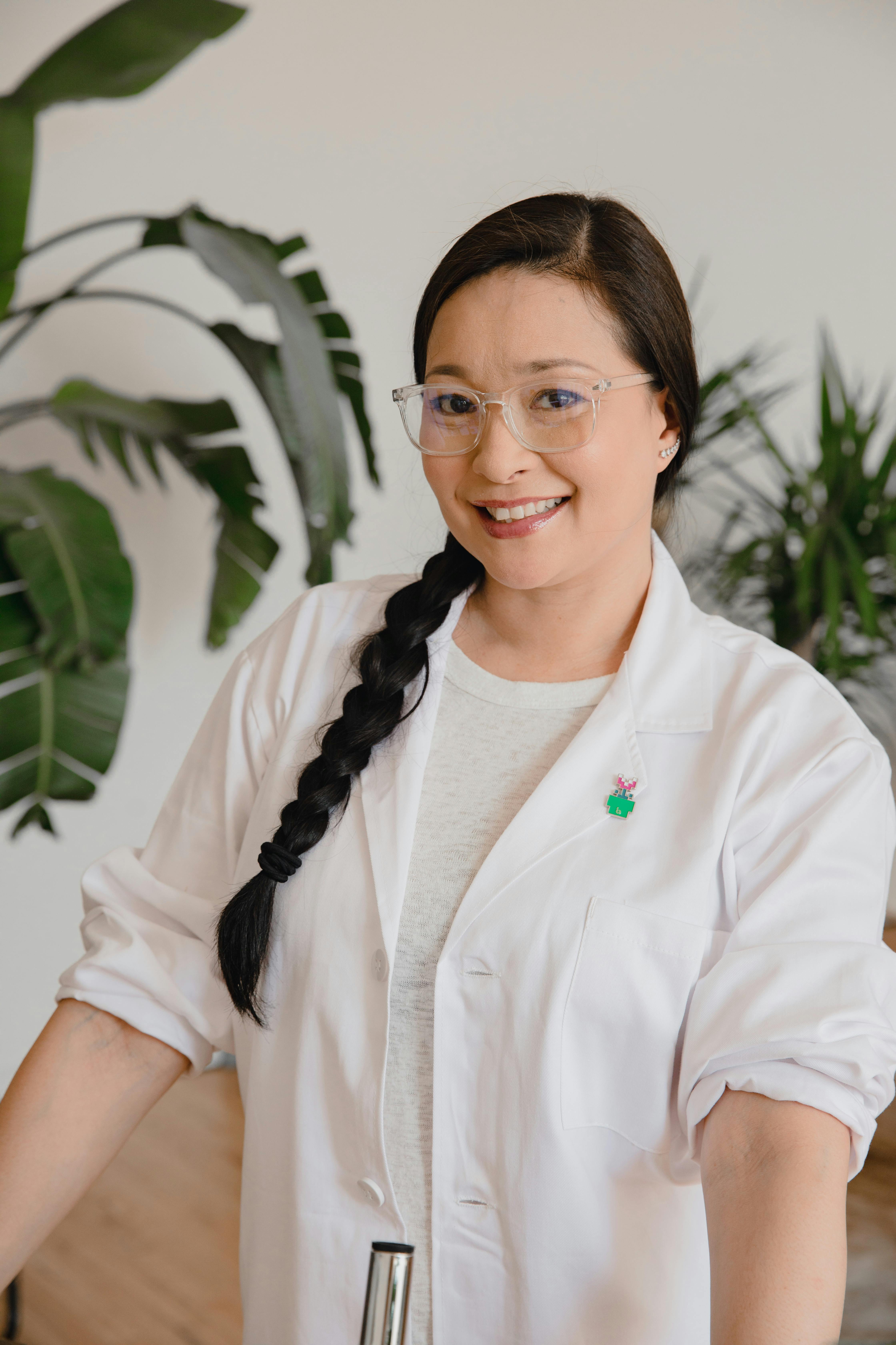 Dr. Elena Rodriguez, Chief Scientist - Asian woman with braided hair smiling confidently in a lab coat, indoors. Photo by RDNE Stock project on Pexels