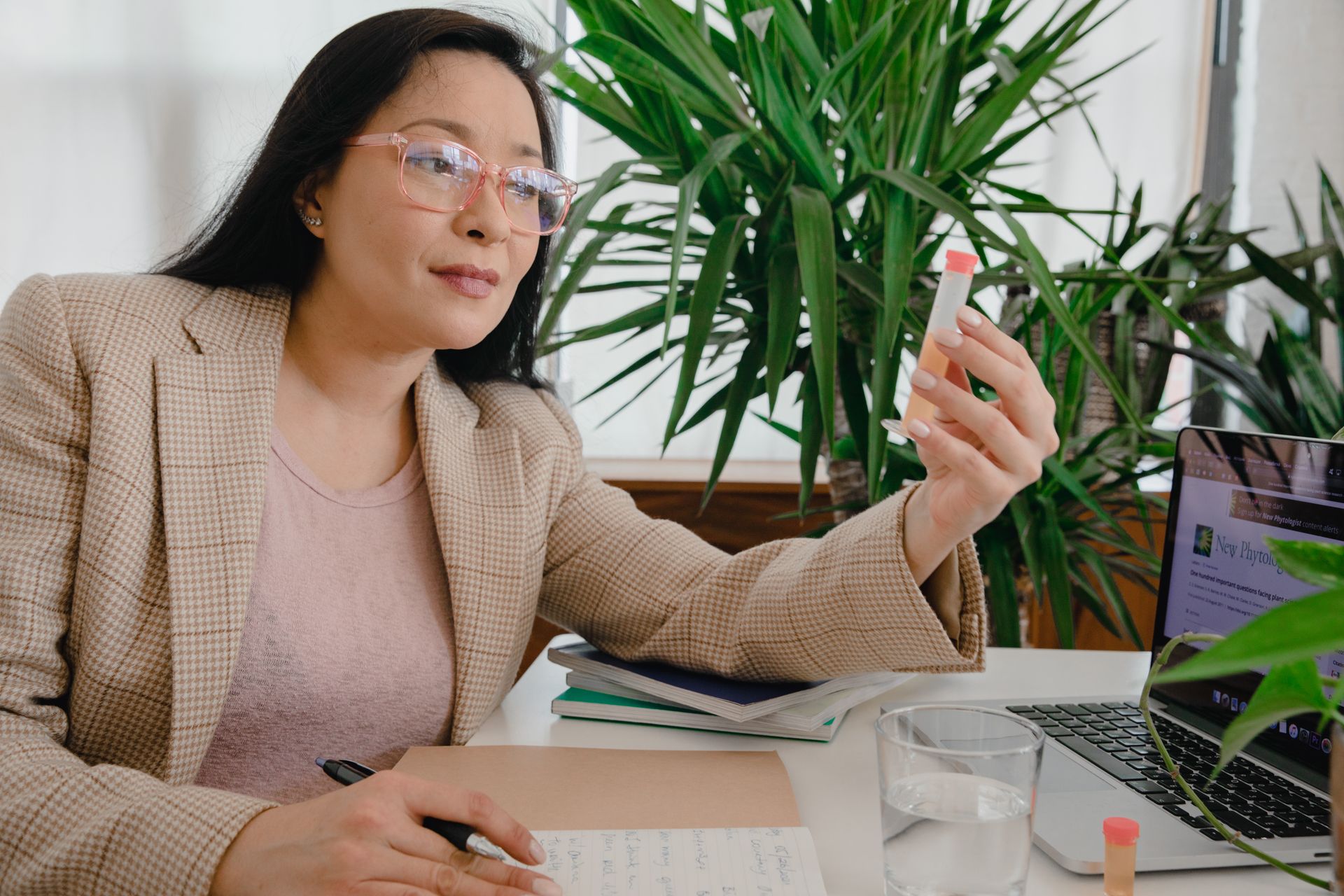 Asian woman in office analyzing a sample while working on a laptop, embodying professionalism and focus.