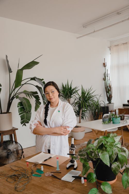 Free Asian female scientist in a lab surrounded by plants, conducting research. Stock Photo