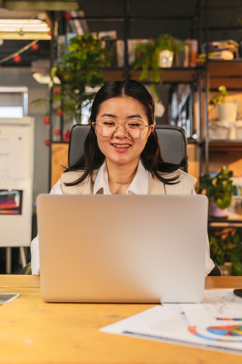 Free Confident businesswoman with eyeglasses using her laptop at a desk in a cozy office setting. Stock Photo
