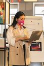 Woman in Beige Coat Wearing Pink Face Mask Using Laptop Computer