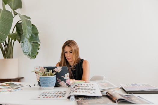 Caucasian woman engaged in work at home with magazines and laptop.