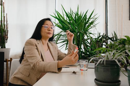 Free Asian woman in office holding a sample tube, surrounded by indoor plants, suggesting a natural environment. Stock Photo
