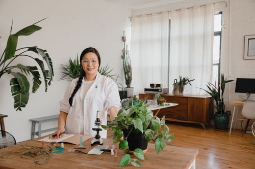 Free Scientist in lab coat with plants and microscope in stylish indoor lab setting. Stock Photo