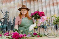 Woman in Green Long Sleeve Shirt and Black Hat Standing Beside Pink Flowers