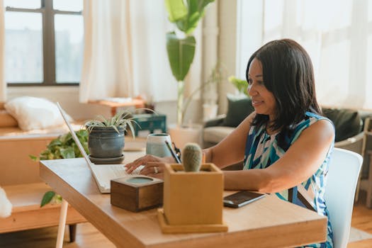 Woman working remotely at home, using laptop, surrounded by plants, creating a cozy workspace.