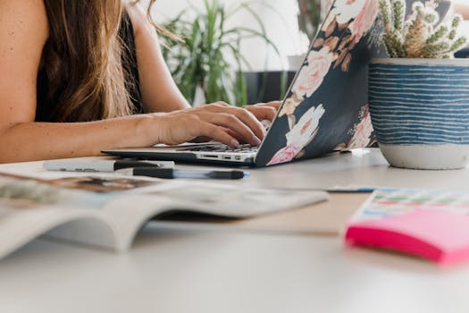 Close-up of a woman typing on a floral laptop in a stylish indoor workspace.
