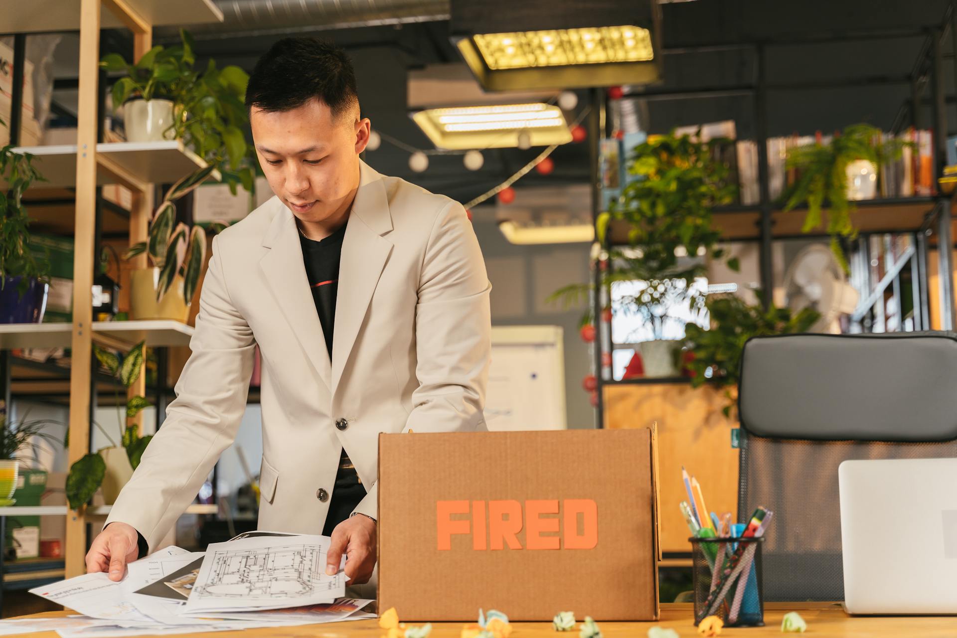 An employee packing documents into a box labeled 'FIRED' in an office environment.