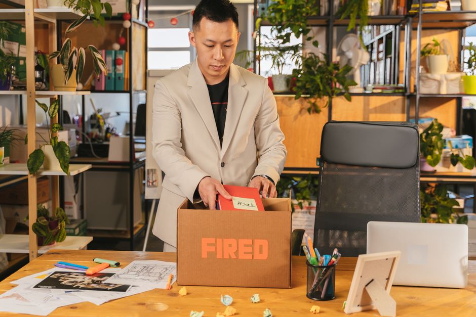 developing adaptability in a rapidly changing job market - An adult man pack personal items after receiving a fired notice in an office setting, expressing corporate life challenges.