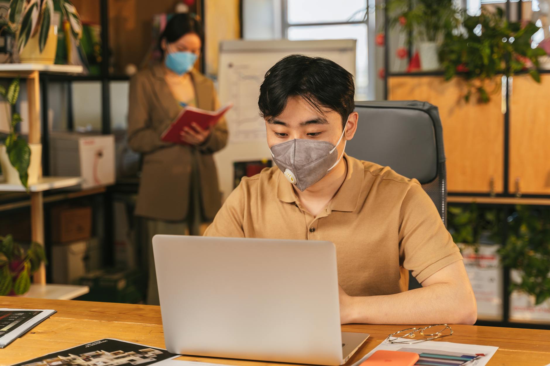 Best Business Management Software for Small Businesses for 2025 | Top Features & Benefits 3 Adult workers in masks collaborating with laptops and notebooks in a modern office setting.