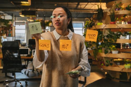 Free Asian woman organizing tasks on sticky notes at modern office workspace. Stock Photo