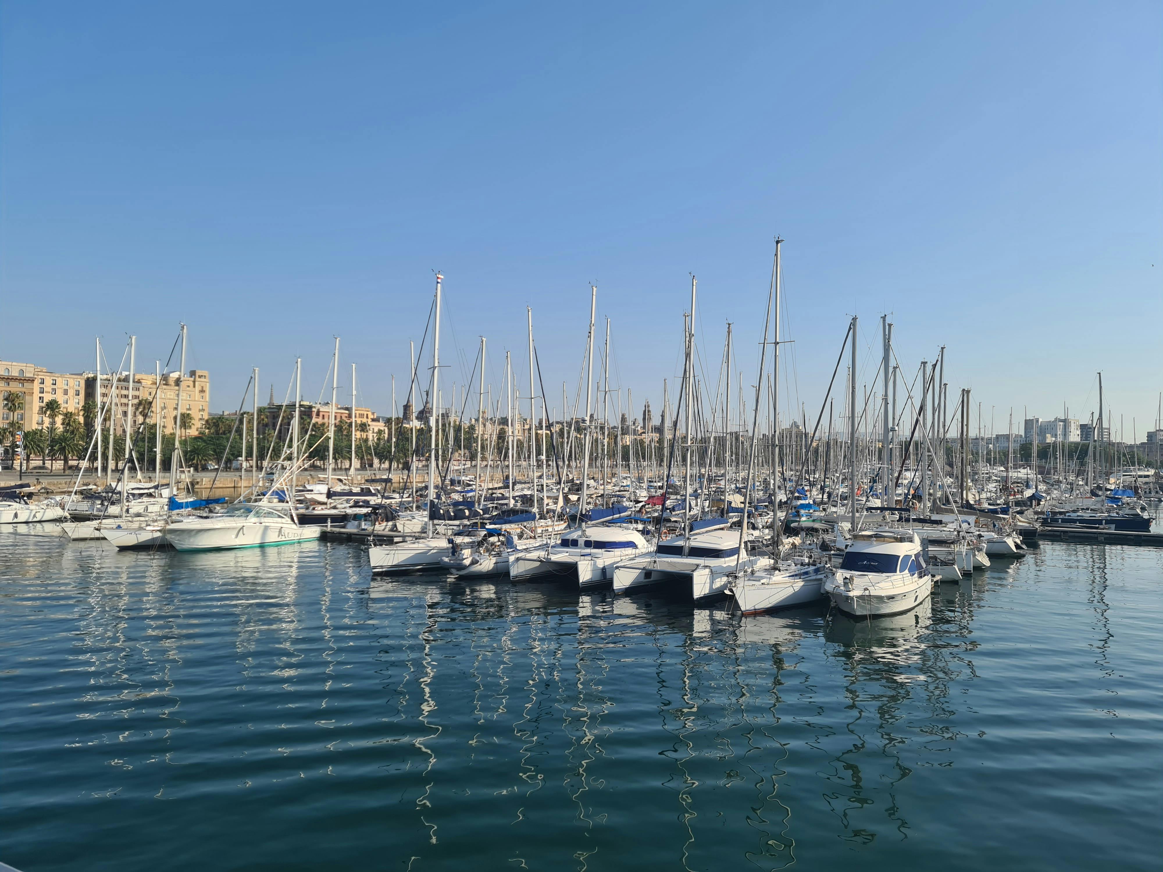 Free A serene view of sailboats docked at a marina against a clear blue sky in Barcelona. Stock Photo