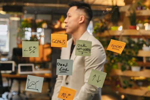Free Asian businessman strategizing with sticky notes on glass in a modern office setting. Stock Photo