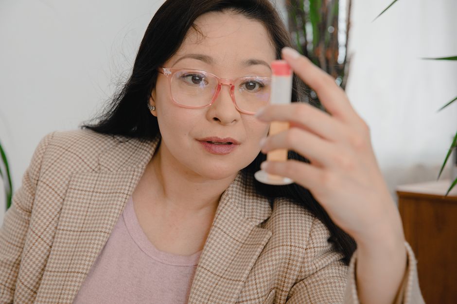 Asian woman wearing glasses observes a plastic container in an office environment.