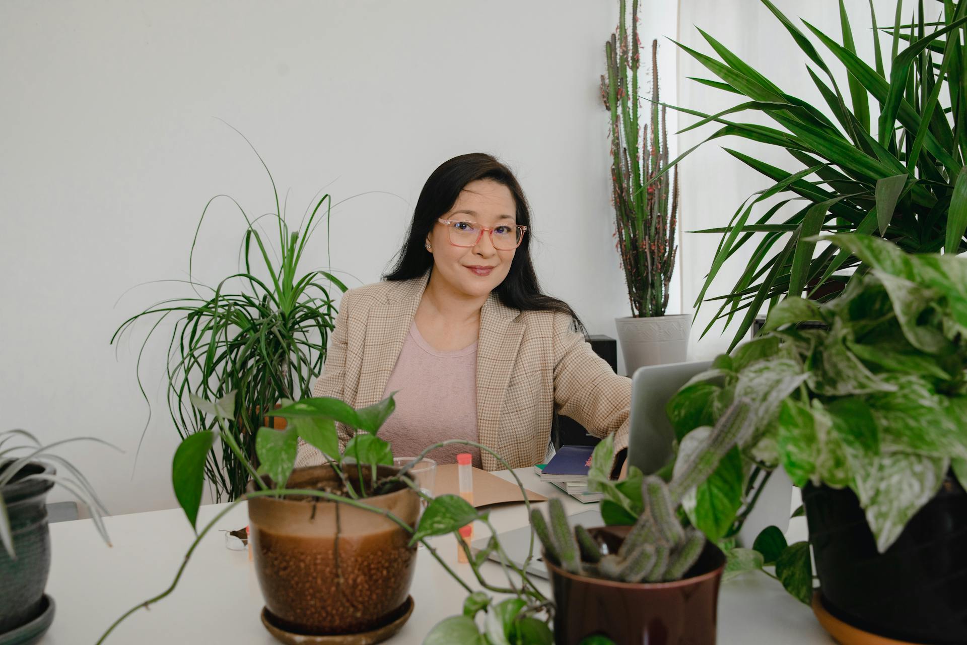 Smiling Asian woman business owner working at a table surrounded by lush houseplants.