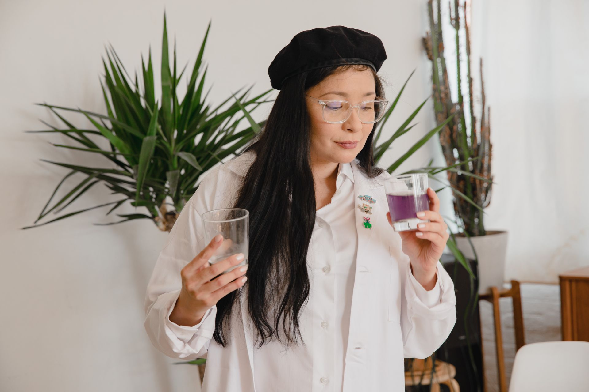 Asian woman in white shirt holding glass of purple juice indoors. Stylish and casual setting.