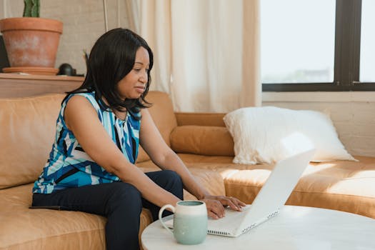 Black woman working on a laptop in a cozy living room setting with natural light.