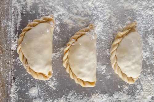 Free Close-up of three freshly prepared empanadas on a floured surface, showcasing homemade baking. Stock Photo