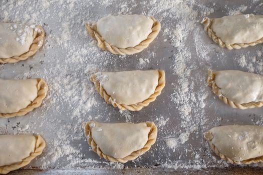 Top-down view of raw empanadas on a floured baking tray ready for baking.