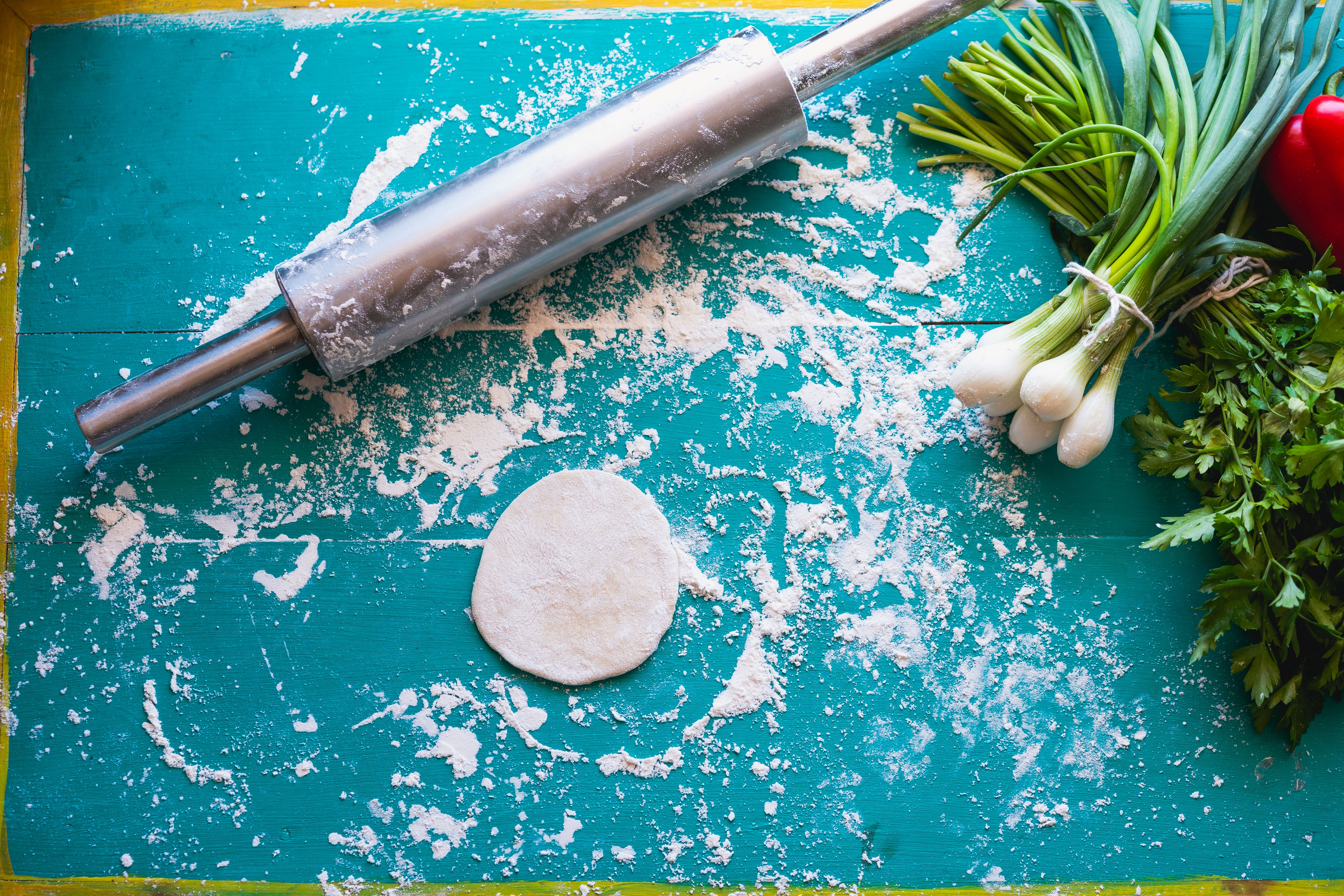 A flat lay of fresh vegetables, dough, and a rolling pin on a vibrant blue surface, ideal for healthy cooking concepts.