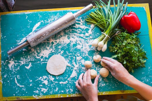 Top view of dough preparation with fresh vegetables and rolling pin on a vibrant table.
