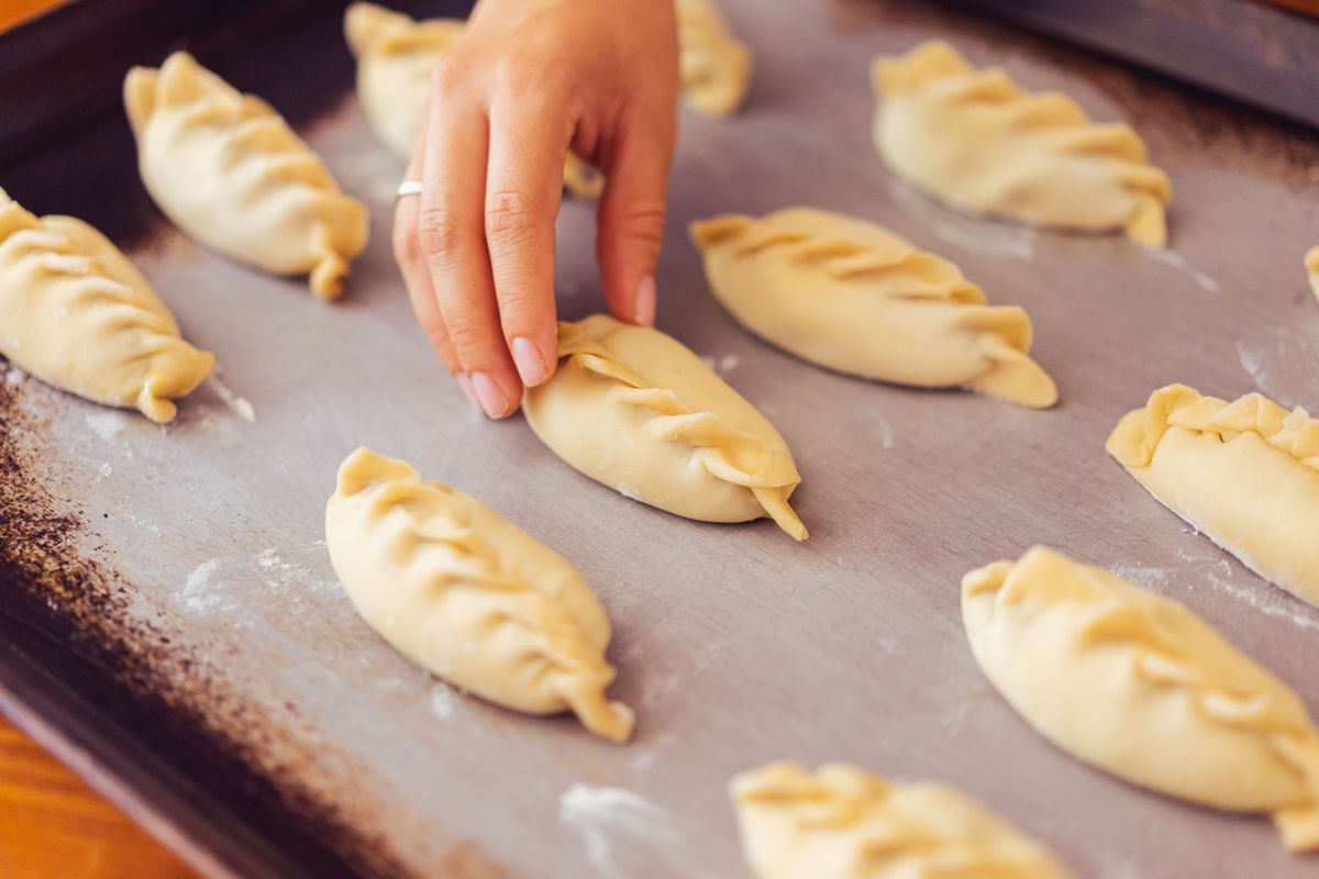 Hands placing raw filled pastries with braided edges on a baking tray