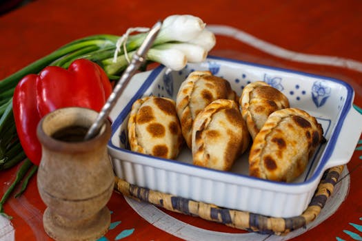 Baked empanadas in a dish with fresh vegetables on a vibrant table.