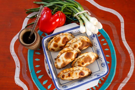 Plate of Argentine empanadas with traditional mate, red pepper, and green onions.