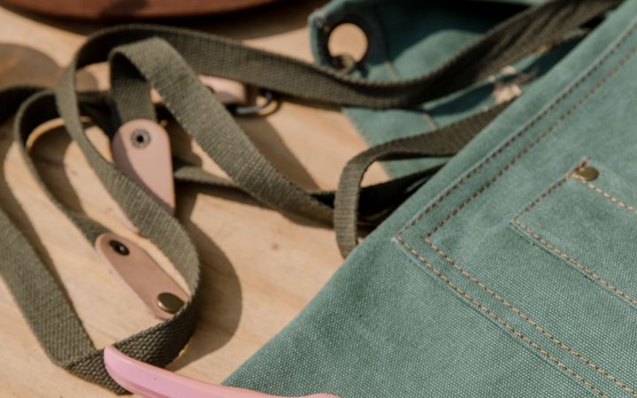Pruning shears and a gardening apron with a hat on a wooden surface, perfect for garden enthusiasts.