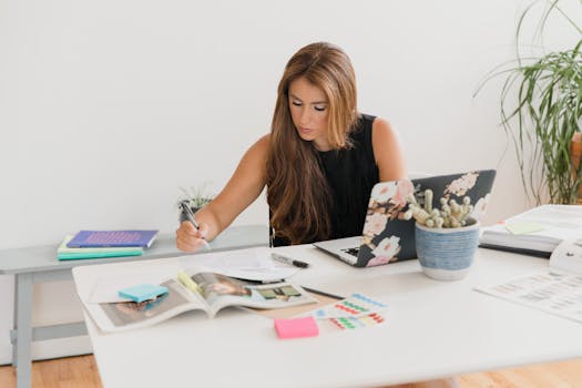 Young businesswoman working diligently at a desk with various materials and a laptop.