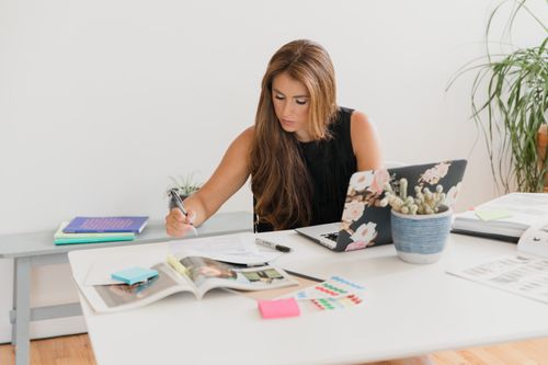 Free Young businesswoman working diligently at a desk with various materials and a laptop. Stock Photo