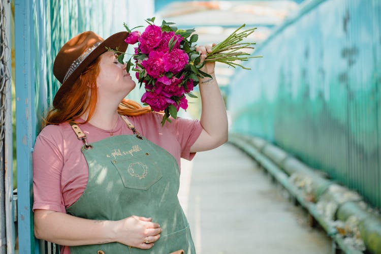 Woman In Pink Shirt And Green Apron Smelling A Bunch Of Flowers