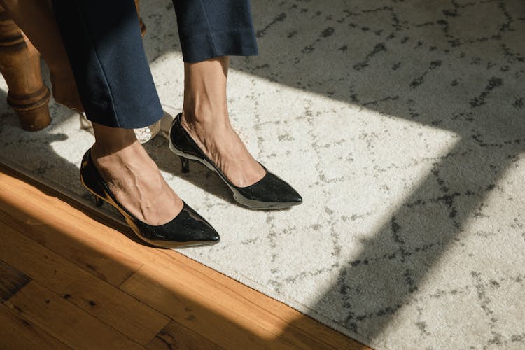 Person Wearing Black Leather Shoes While Standing On A A Floor With Carpet