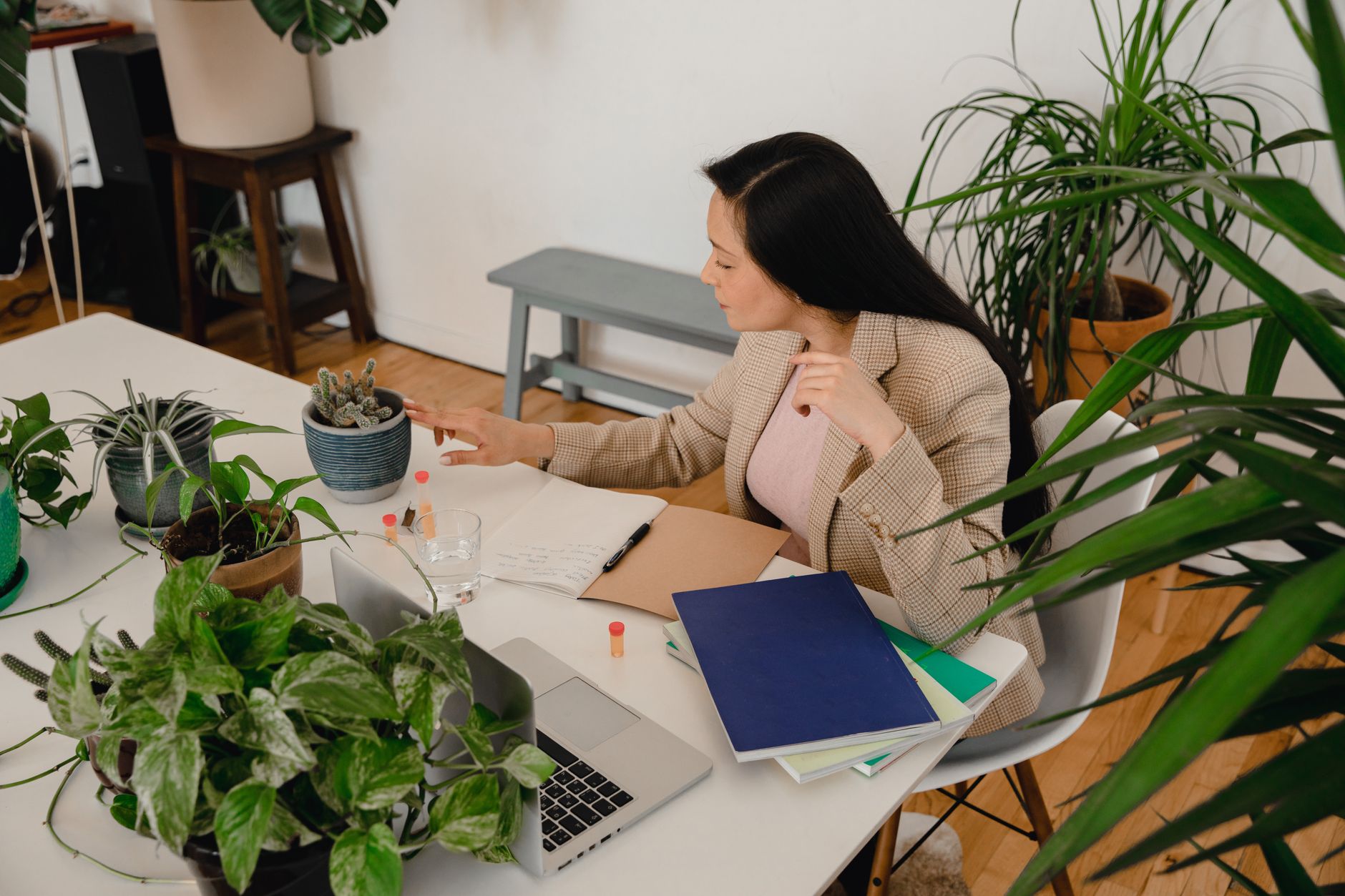 A woman working at a desk with a laptop, notebooks, and plants, representing focused cognitive work