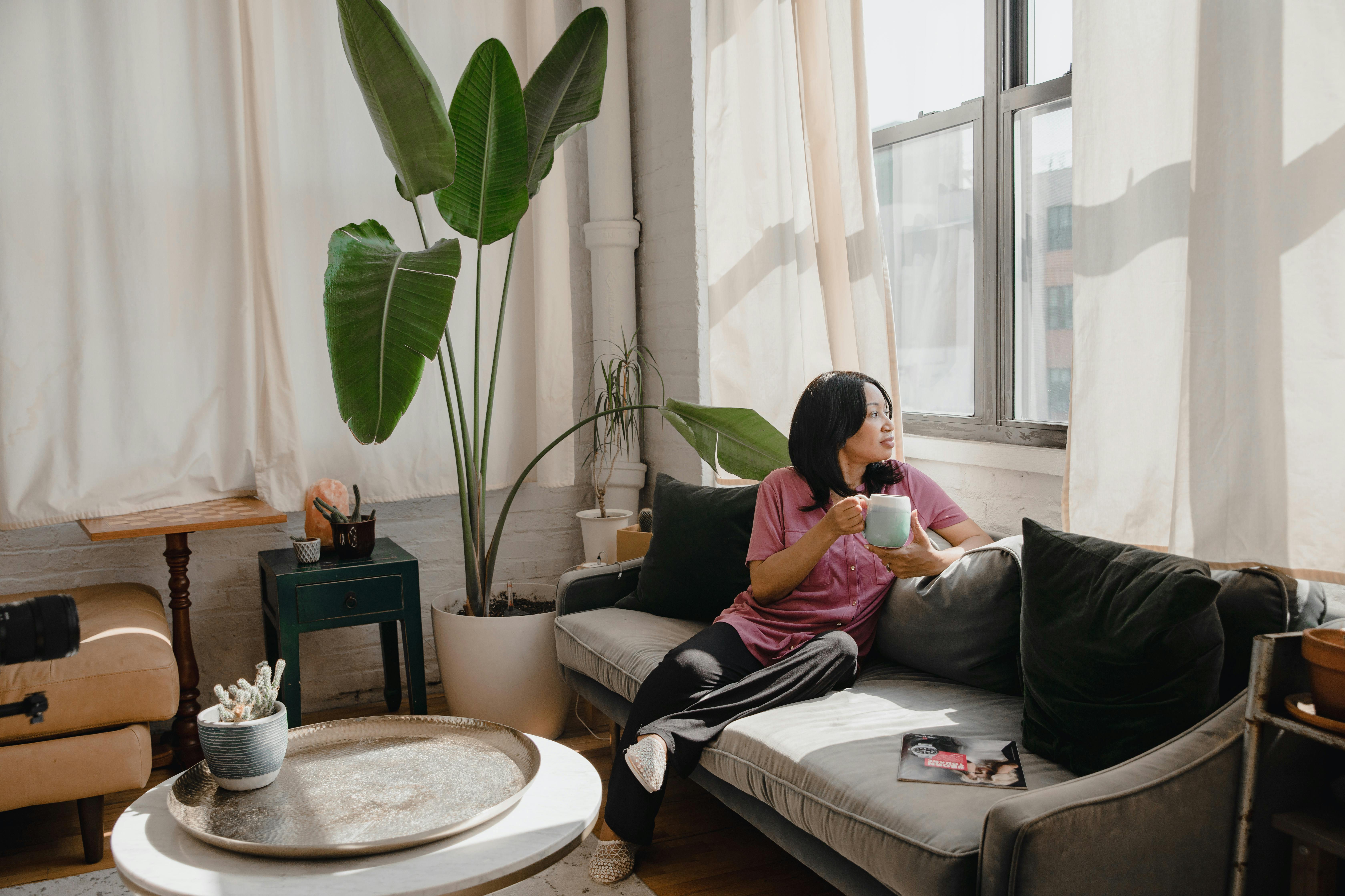 Woman Sitting On A Couch Looking Exhausted With Coffee Cup Nearby