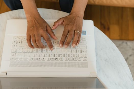 Close-up of hands typing on a white laptop on a marble table. Perfect for tech and work-from-home themes.