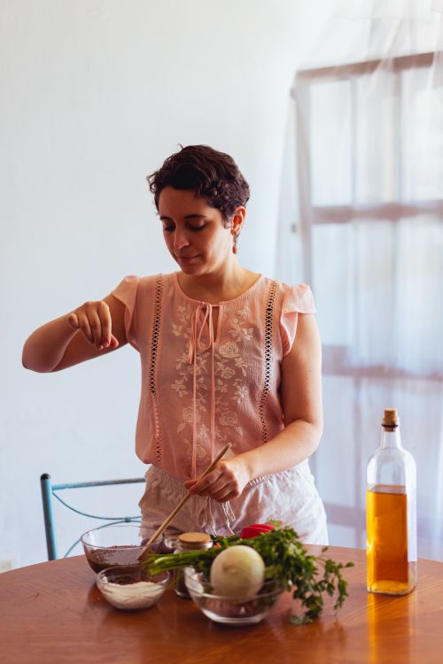 Free A woman sprinkles seasoning over a bowl while preparing a meal at home. Stock Photo