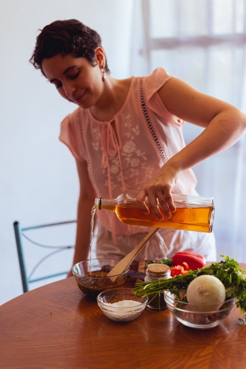 Free Hispanic woman pouring olive oil into a bowl while preparing a fresh meal in the kitchen. Stock Photo