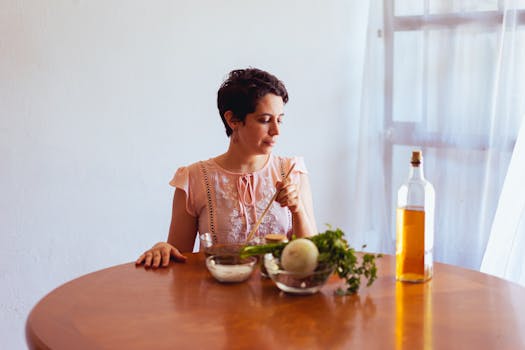 Woman in light dress preparing fresh ingredients with oil indoors.