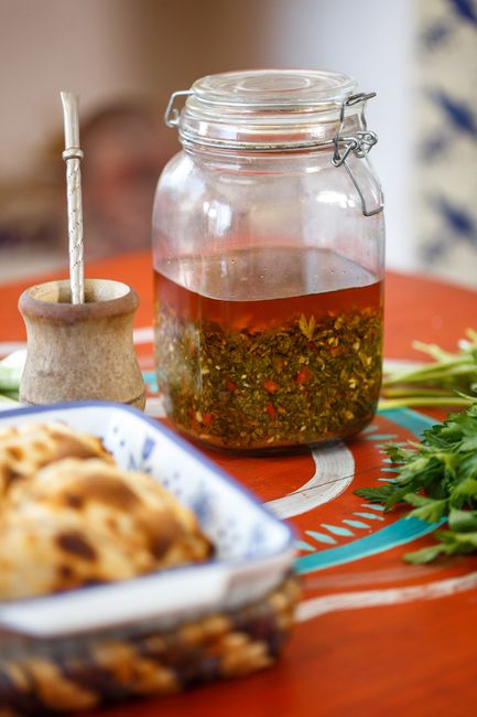 A small glass jar filled with whole golden garlic cloves submerged in olive oil, with a few cloves spooned onto a piece of toasted bread beside it.