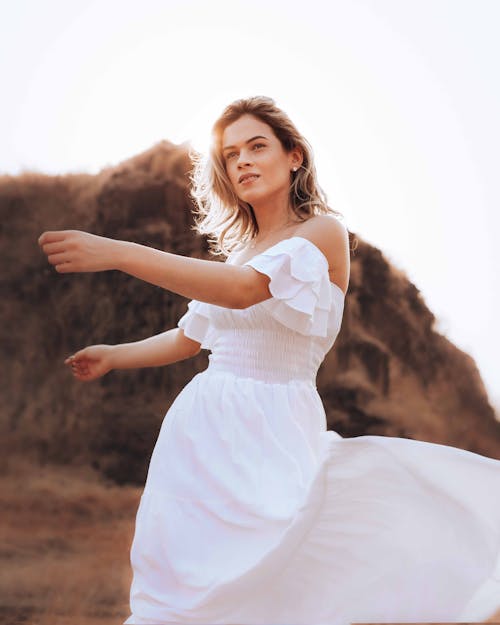 Young gentle woman in bridal dress dancing while looking away against mount on wedding day in back lit