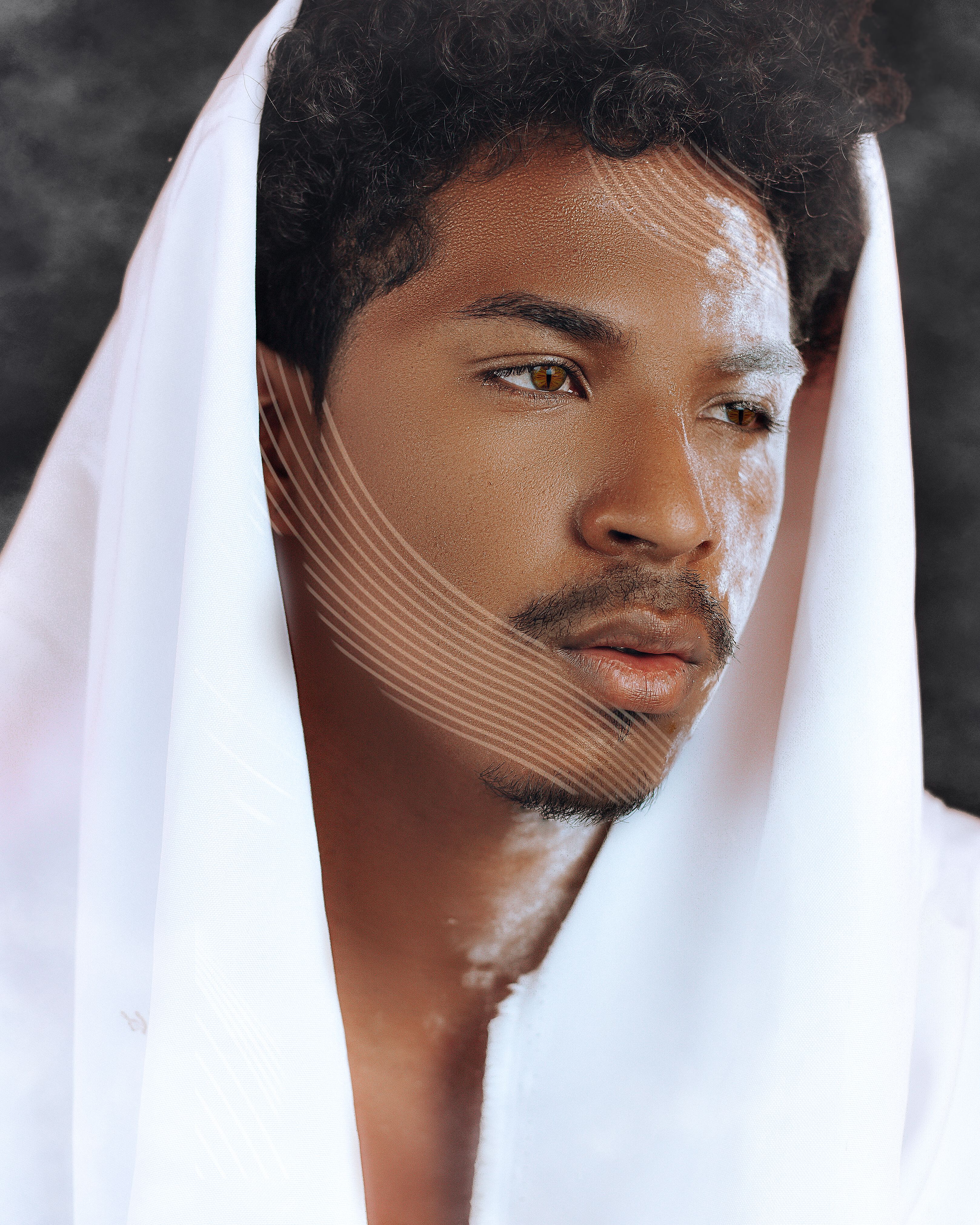 Contemplative ethnic male with white fabric on curly hair and geometric makeup on cheek and forehead looking away